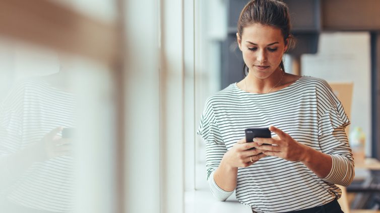 Woman standing beside a window holding mobile phone.