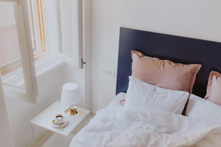 White bedroom interior with window, coffee and small lamp on side table - Image Via kaboompics - By KAROLINA GRABOWSKA