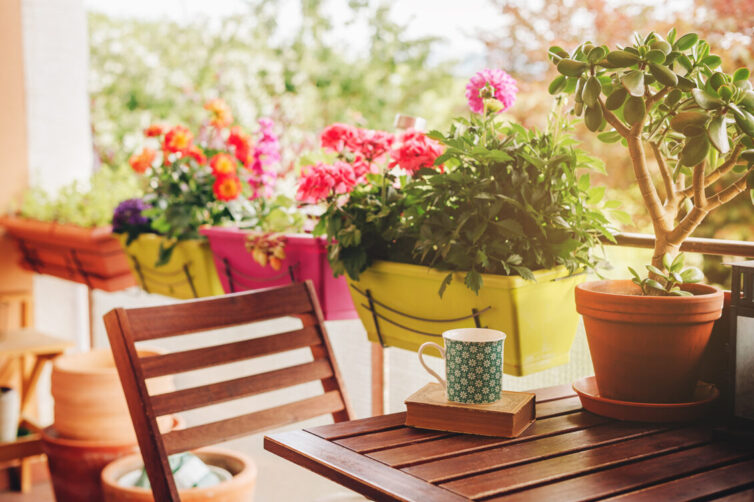 Balcony with wooden table and chairs and bright coloured planters full of plants