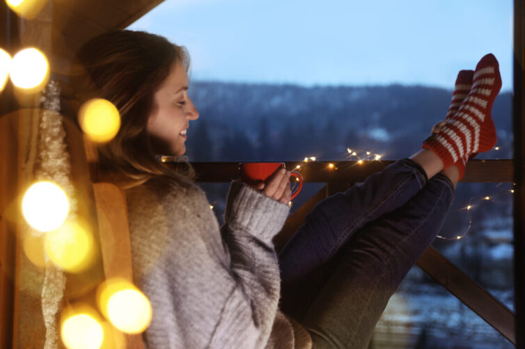 Women in jumper sat on balcony with hot drink and fairy lights