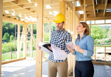 Man with hard hat and women walking around a building site. Wooden home