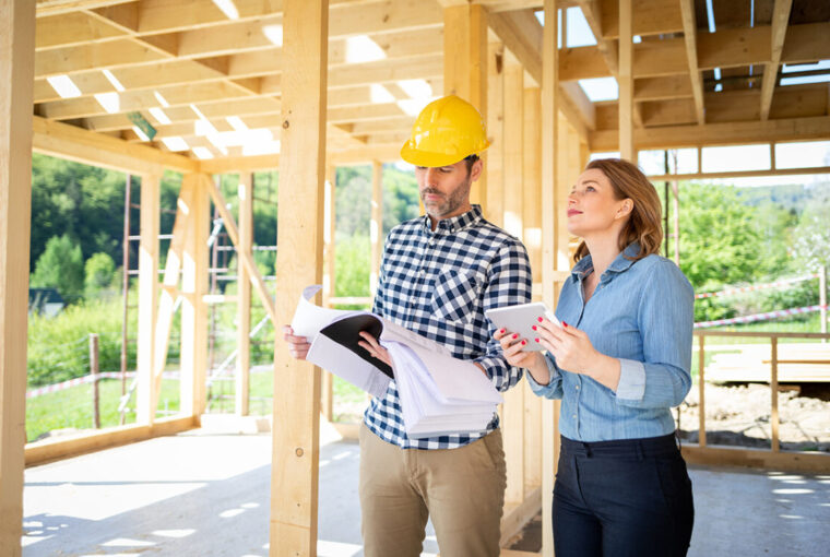 Man with hard hat and women walking around a building site. Wooden home