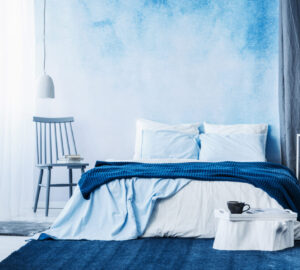 Navy blue carpet in minimal bedroom interior with blanket on bed next to a chair and under a lamp