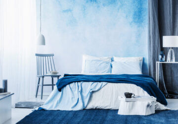Navy blue carpet in minimal bedroom interior with blanket on bed next to a chair and under a lamp