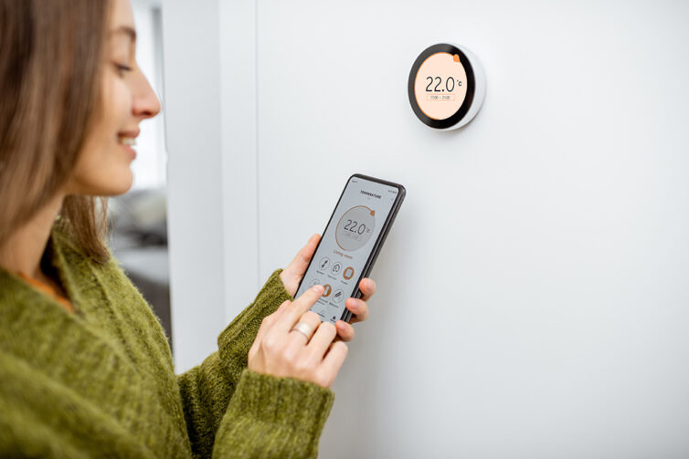 Woman regulating heating temperature with a modern wireless thermostat and smart phone.