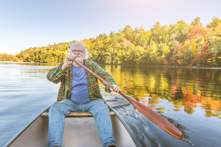 Elderly man with canoe at lake on a sunny autumn day