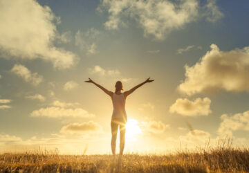 Women with arms in air embracing beautiful scenery and looking at the sky