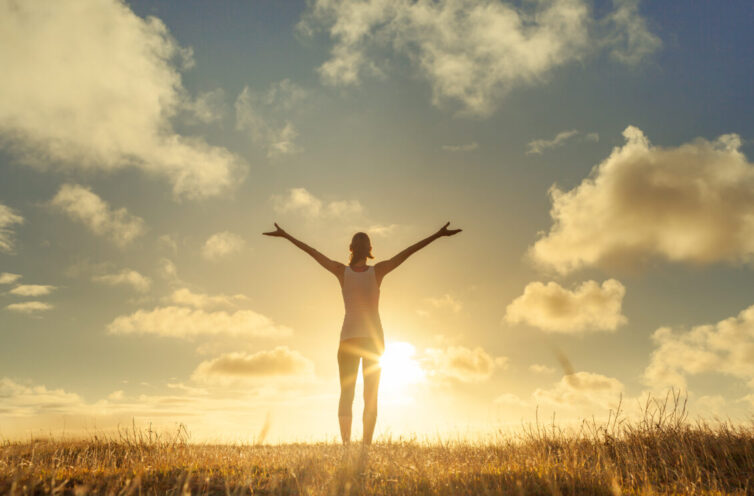 Women with arms in air embracing beautiful scenery and looking at the sky