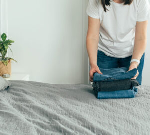 Woman folding clothes/ jeans in clutter free bedroom