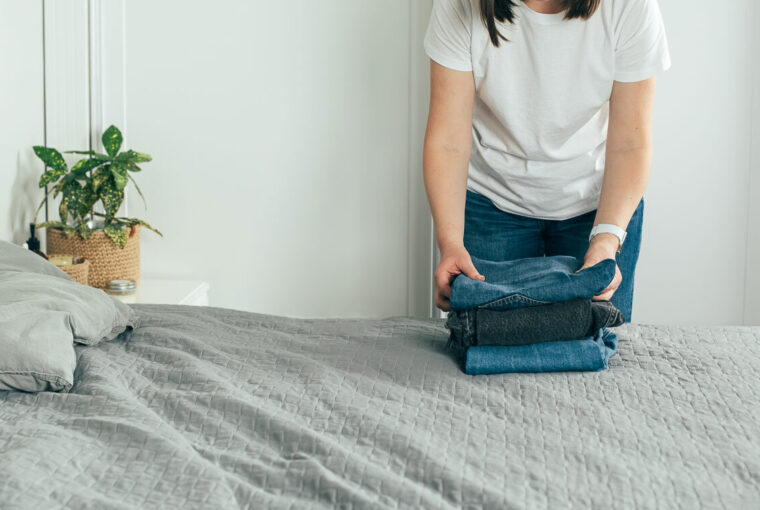 Woman folding clothes/ jeans in clutter free bedroom
