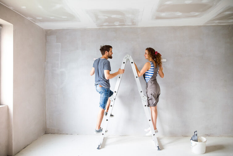 Couple standing on ladders painting plastered walls
