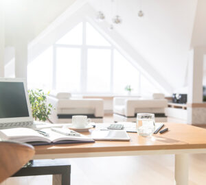 Bright open plan apartment with white sofa and home office with desk, chair and laptop.