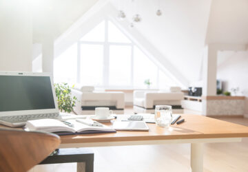 Bright open plan apartment with white sofa and home office with desk, chair and laptop.