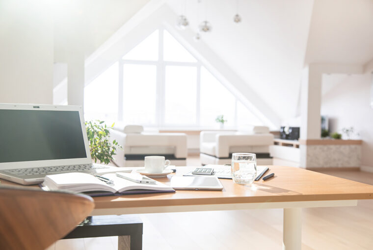 Bright open plan apartment with white sofa and home office with desk, chair and laptop.