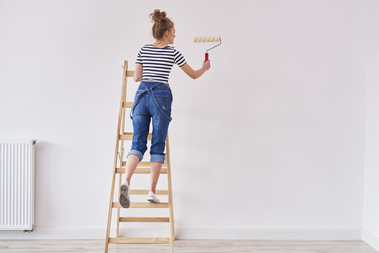 Women on a wooden step ladder painting wall