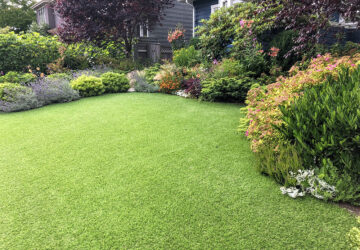 artificial lawn in the front yard with nice flowers and shrubs surrounding it