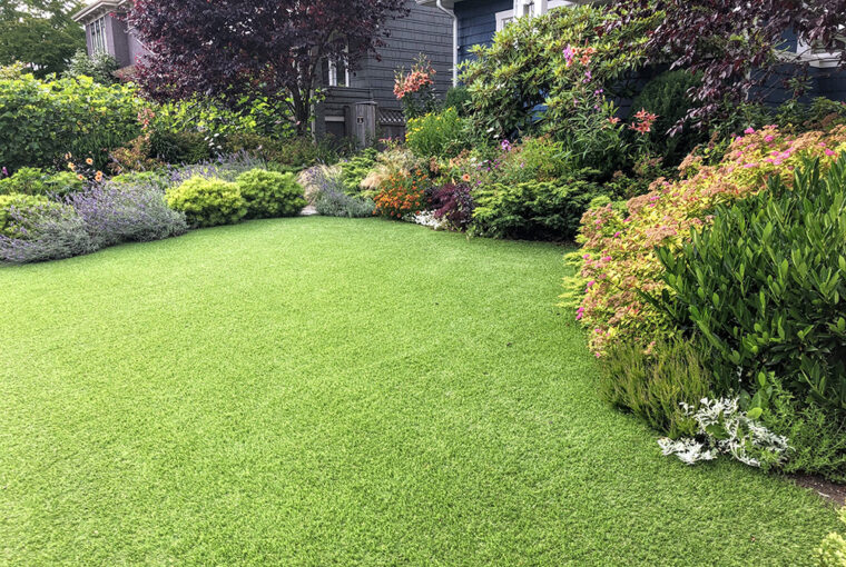 artificial lawn in the front yard with nice flowers and shrubs surrounding it