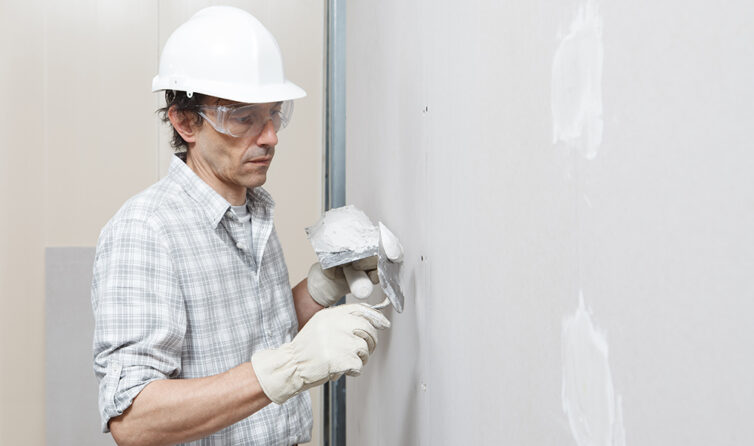 Man wearing hard hat filling in holes in the wall