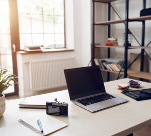 Home office with large windows, desk, shelving and laptop.