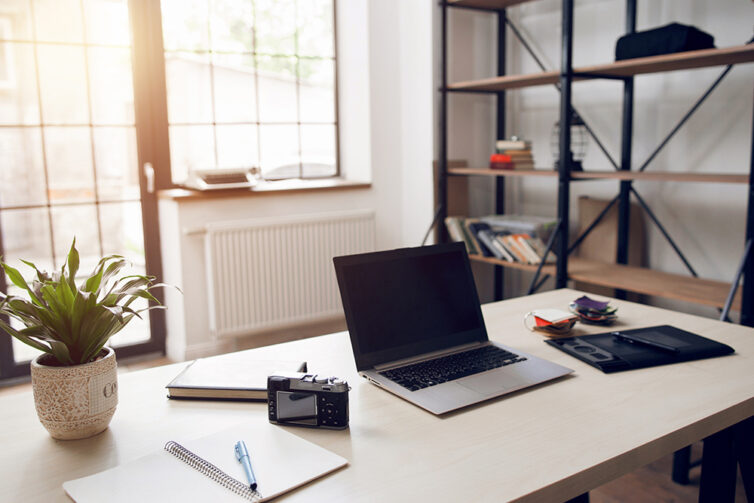 Home office with large windows, desk, shelving and laptop.