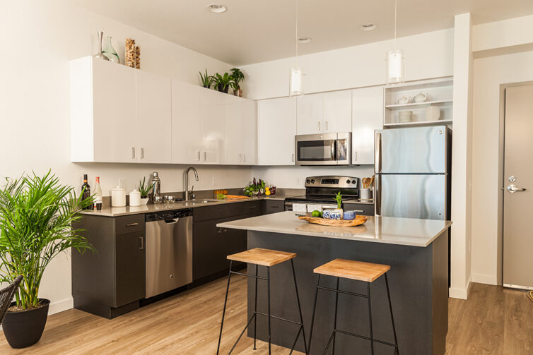 Modern dark kitchen cabinets with laminate flooring, bar stools and white worktops