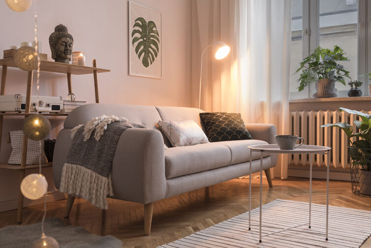 Cosy lounge with grey sofa, cushions, drapped blanket, and warm lighting