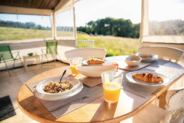 Glamping in large tent Breakfast table set and laid with bowls of cereal and a glass of orange fruit juice.