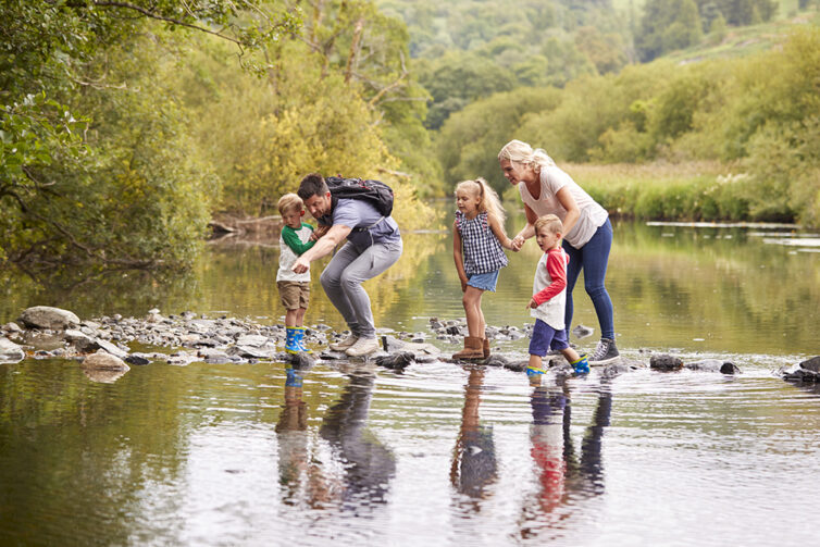 Family on holiday in the Lake District UK. Family crossing river via rocks in the water