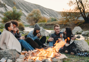 Group sat around bonfire drinking hot drinks.
