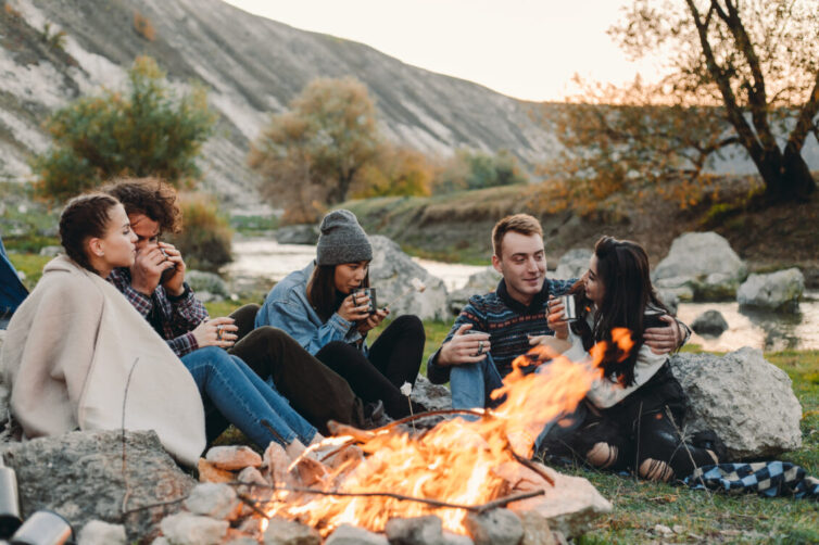 Group sat around bonfire drinking hot drinks.