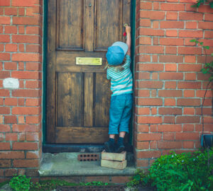 Child standing on bricks to unlock front door
