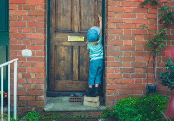 Child standing on bricks to unlock front door