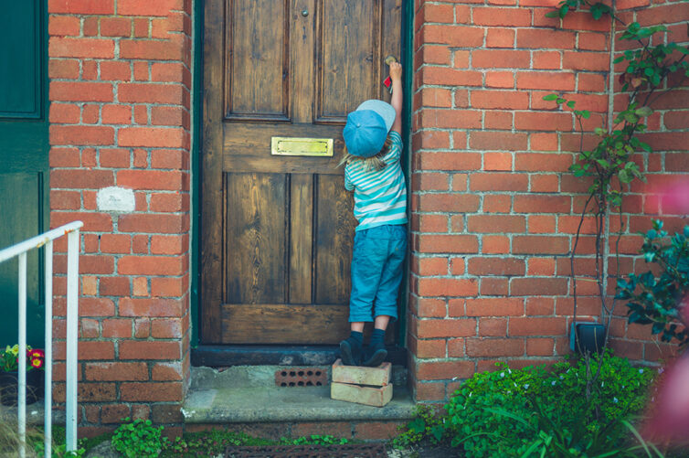 Child standing on bricks to unlock front door