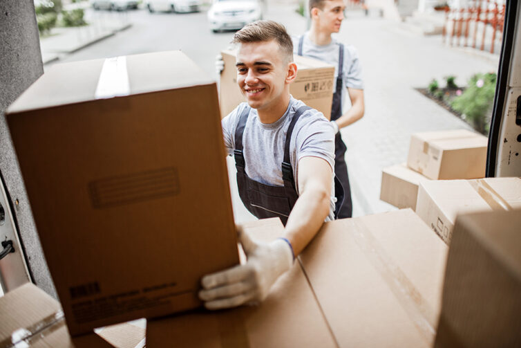 Smiling removal men in overalls carrying boxes