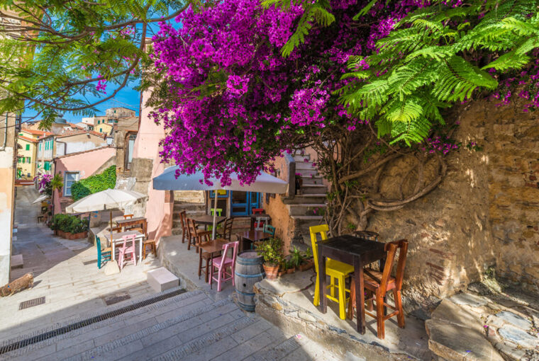 Street with cafe table and chairs. Flowers in bloom in Capoliveri village in Elba island, Tuscany, Italy, Europe