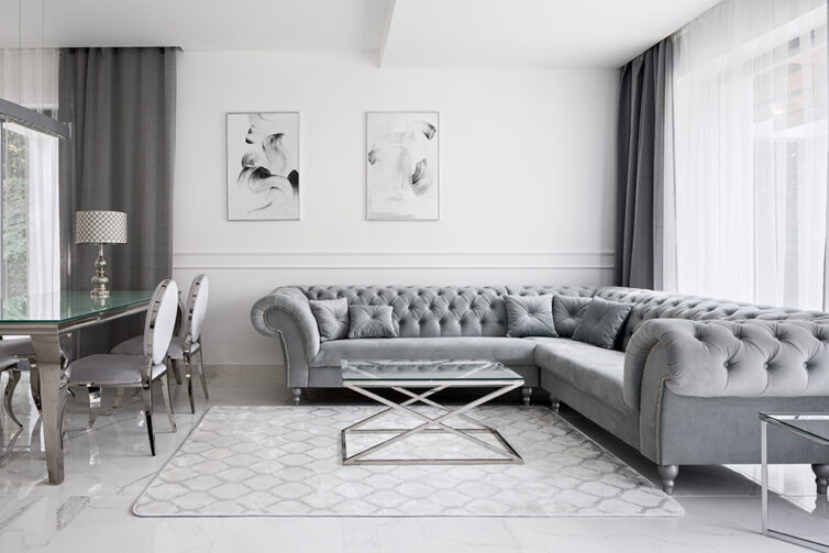 Minimalist opulent living room. Large chesterfield silver corner sofa, glass coffee table and dining table