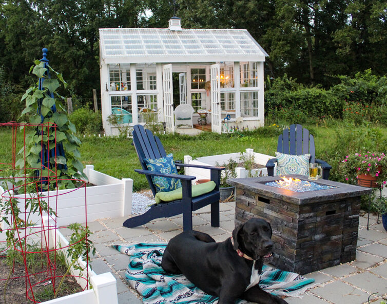 Garden with large white greenhouse, Adirondack Chairs, firepit and large black dog.