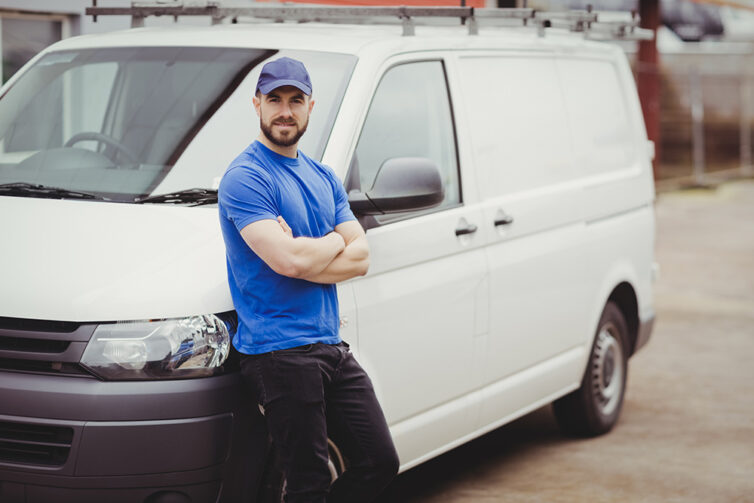 Engineer in blue t-shirt standing next to white van