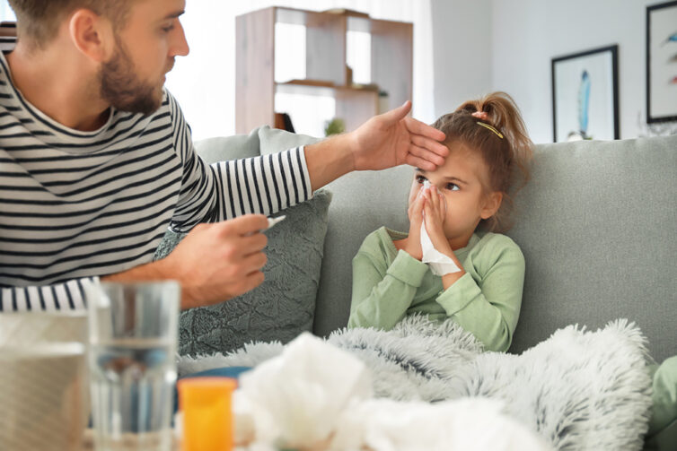 Child with a cold blowing nose. Dad checking temperature of daughter.