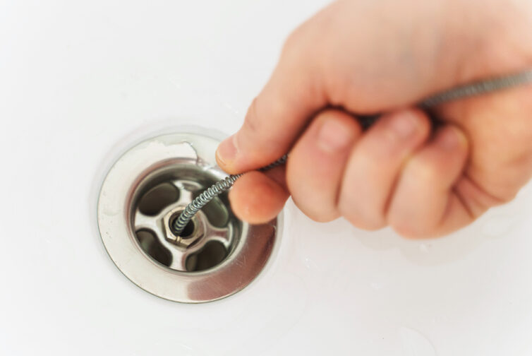 Plumber using drain snake to unclog bathtub