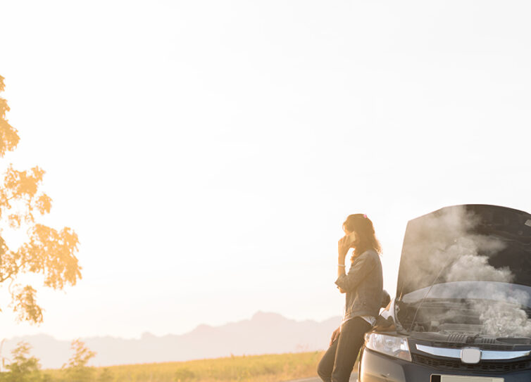 Women leaning against broken down car with steam coming out of the engine