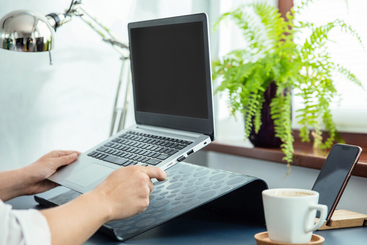 Laptop being placed onto black laptop stand. Home office with plants.