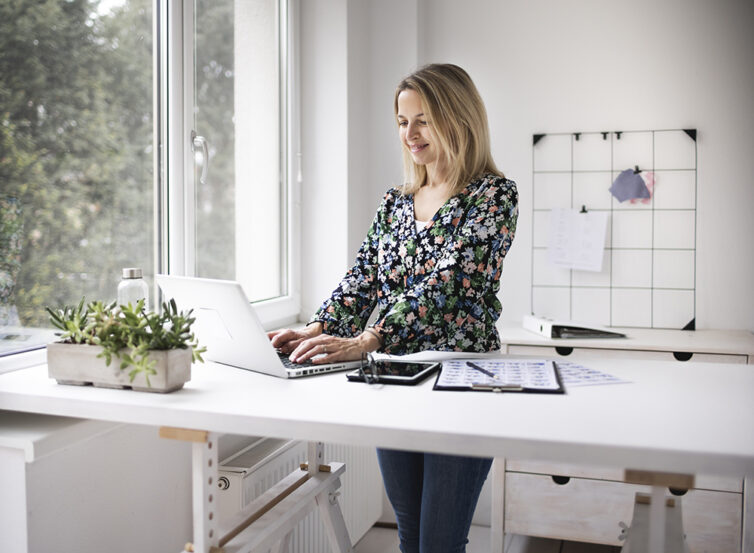 Women using standing desk with laptop. Ergonomic Home Office.