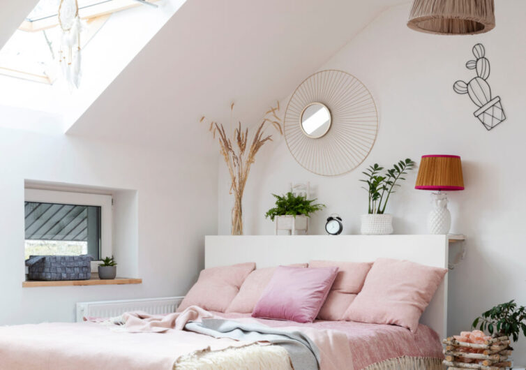 Pink and white bedroom with plant and lamp place on top of the headboard