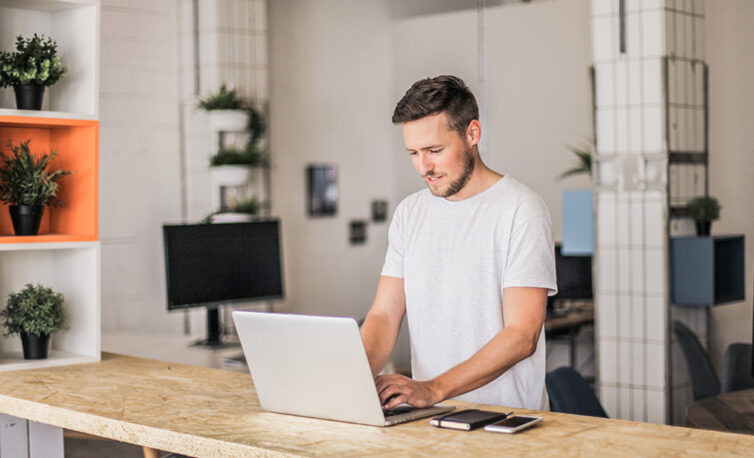 Man working in office at a standing desk, using his laptop.