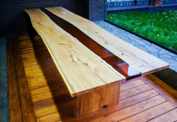 Large long wooden table with epoxy design in the middle. Placed in room with large floor to ceiling window