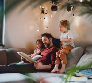 Dad, daughter and son sat on sofa. Fairy lights on the wall.