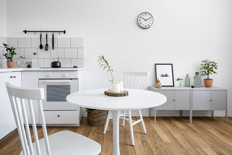 White kichen with white round dining table and white chairs. Wooden flooring and grey sideboard