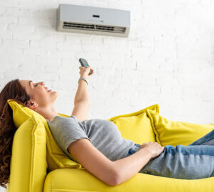 Women on yellow sofa pressing remote control to air conditioning unit