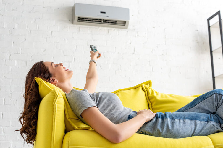 Women on yellow sofa pressing remote control to air conditioning unit